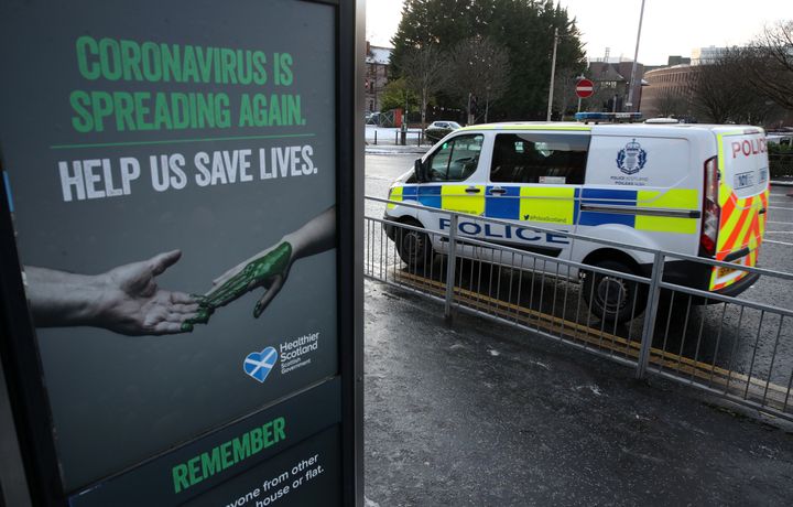 A police vehicles passes a Coronavirus related poster on a phone box outside Glasgow Royal Infirmary