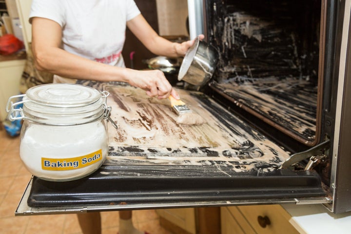 Person applying mixed baking soda onto surface of oven for effective and safe cleaning