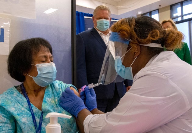 Ontario Premier Doug Ford looks on as the second dose of the Pfizer-BioNTech COVID-19 vaccine in Canada is administered to personal support worker Anita Quidangen by registered nurse Hiwot Arfaso at The Michener Institute in Toronto on Jan. 4, 2021.