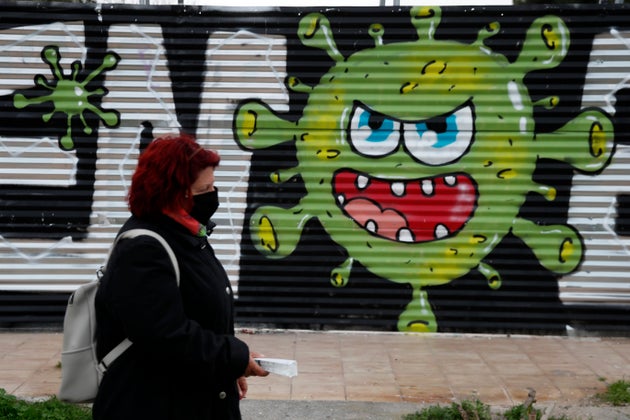 A woman wearing a face mask to prevent the spread of coronavirus, walks in front of a graffiti by artists Open/Esem in Athens, Tuesday, Jan. 12, 2021. Greece has extended a two-month lockdown till Jan. 18, and announced plans to increase the number of people getting COVID-19 vaccines. (AP Photo/Thanassis Stavrakis)