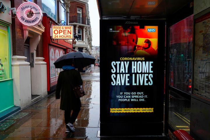 A pedestrians walks past NHS signage promoting "Stay Home, Save Lives" on a bus shelter in London 