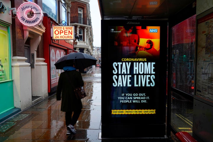 A pedestrians walks past NHS signage promoting "Stay Home, Save Lives" on a bus shelter in London