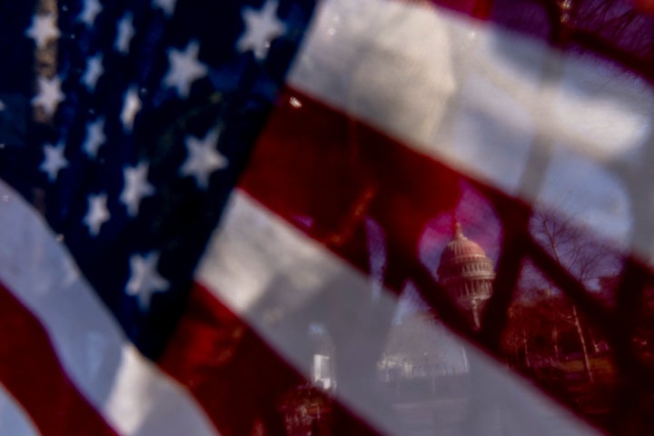 The dome of the U.S. Capitol is visible through an American flag placed on fencing surrounding the Capitol Building on Capitol Hill in Washington, Thursday, Jan. 14, 2021. (AP Photo/Andrew Harnik)