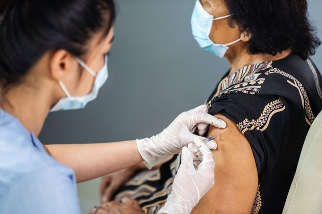 doctor in gloves holding syringe and making injection to senior patient in medical mask