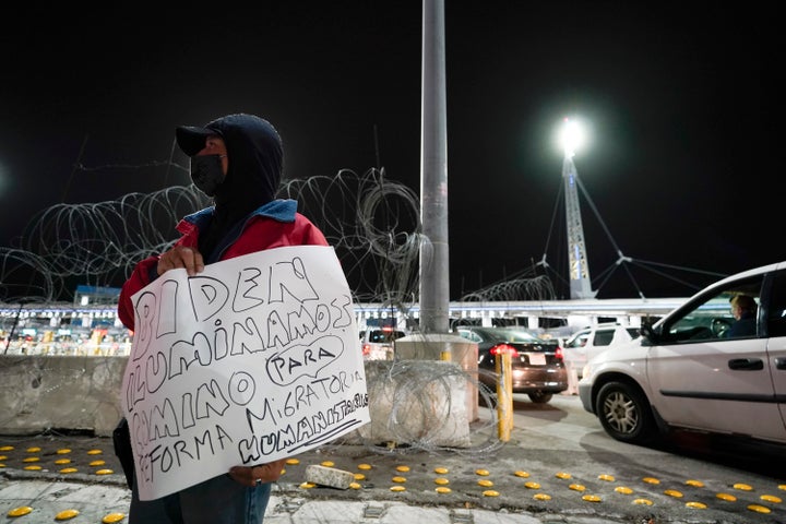 A man holds a sign during a vigil in support of migrants as he stands at the entrance to the San Ysidro Port of Entry along the border between the United States and Mexico, late Tuesday, Jan. 19, 2021, in Tijuana, Mexico. President-elect Joe Biden plans to unveil a sweeping immigration bill on Day One of his administration. It would provide an eight-year path to citizenship for an estimated 11 million people living in the U.S. without legal status, according to a person granted anonymity to discuss the legislation. (AP Photo/Gregory Bull)