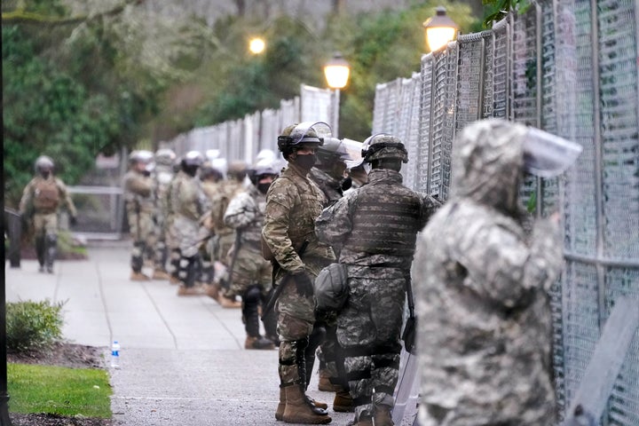 Des membres de la Garde nationale de Washington se tiennent devant une clôture entourant le Capitole en prévision des manifestations du 11 janvier 2021 à Olympia, Washington. Les capitales des États à travers le pays ont été placées sous haute sécurité après l’assaut du Capitole. 