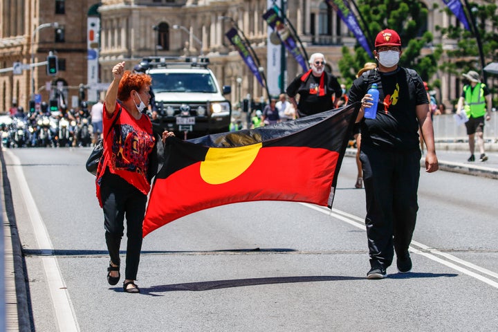 Protesters hold the Aboriginal Flag across Victoria Bridge during the rally. 