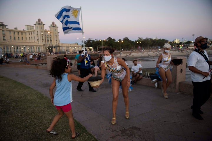 A girl hands over a coin to a Candombe artist performing at the Rambla of Montevideo, Uruguay, on Jan. 23, 2021. Countries wi