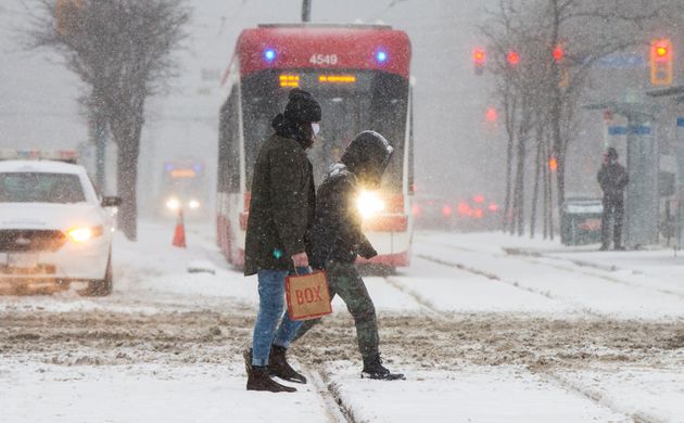 People wearing face masks cross a street during a snowfall in Toronto, Jan. 26,