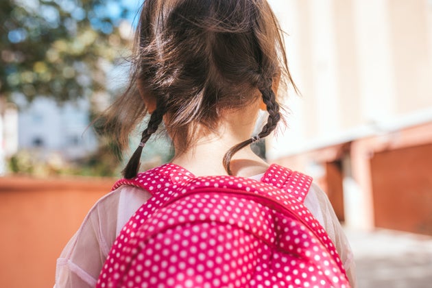 Closeup rear view portrait of cute little girl preschooler posing outdoor with pink backpack against blurred building. Happy kid toodler girl walking after learning school lessons. People, education