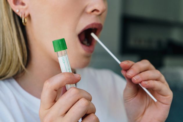 Young woman  holds a swab into her mouth and holding a medical tube for the coronavirus / covid19 home test