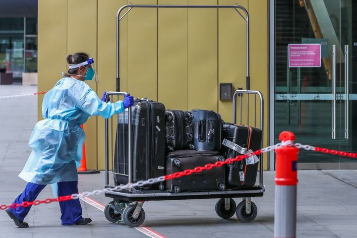 A hotel quarantine staff member is seen wearing full PPE gear while pushing a luggage trolley prior to entering a complex in Melbourne 