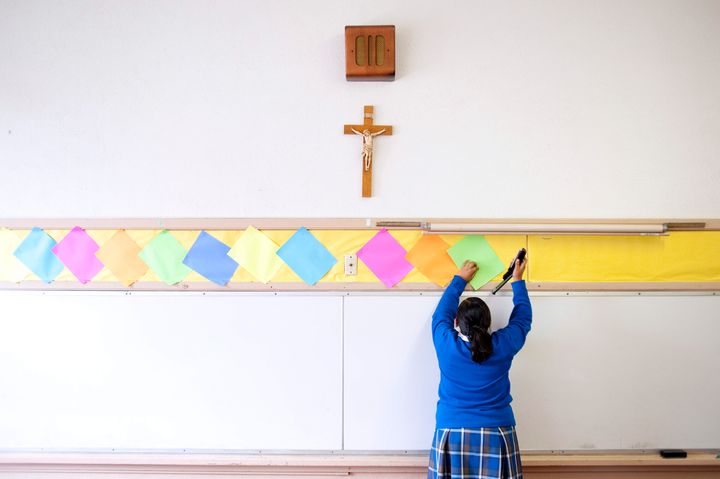 A photo from July 2012 shows a student stapling colored paper to the wall of a classroom at Our Lady of Lourdes in Los Angele