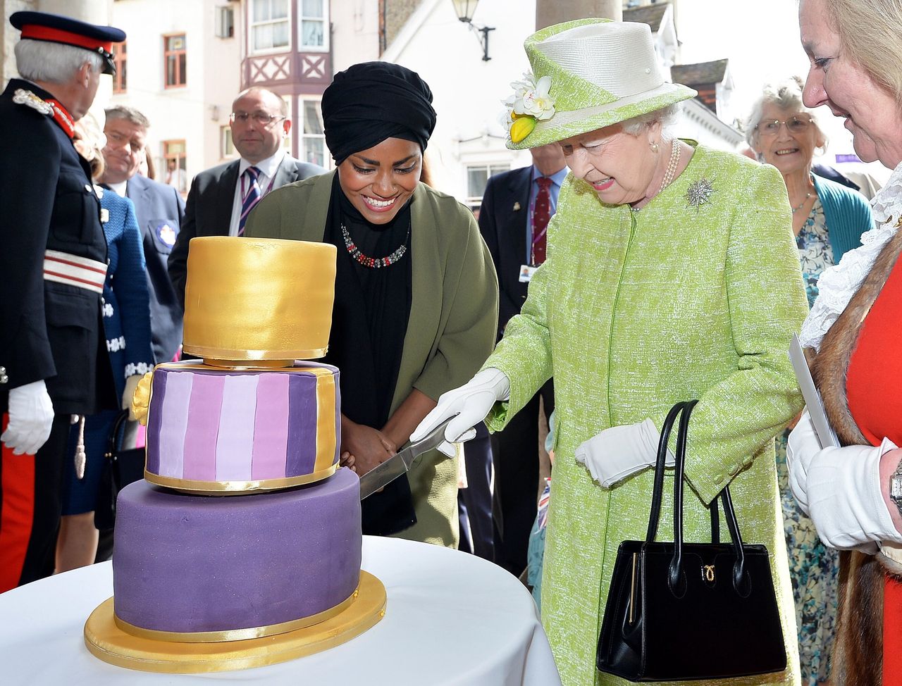 Queen Elizabeth II cuts into a birthday cake baked by Nadiya Hussain, left, during the queen's 90th birthday celebration in April 2016.