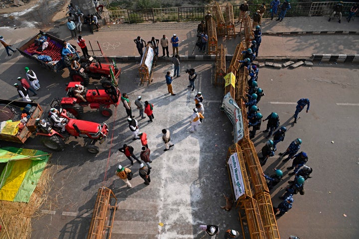 Indian farmers gather next to their tractors as police stand guard at a road block to stop them from marching to New Delhi to protest against the central government's recent agricultural reforms on Dec.1, 2020.