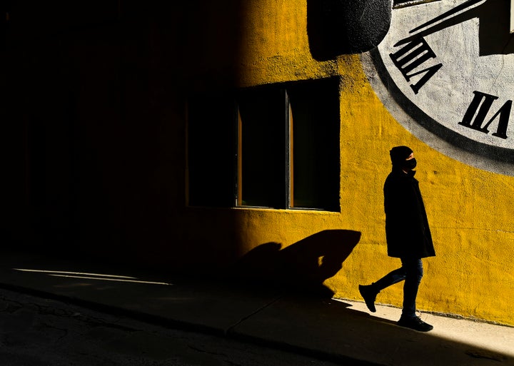 A man wearing a protective mask walks into the sunlight in Toronto on Feb. 11, 2021. 