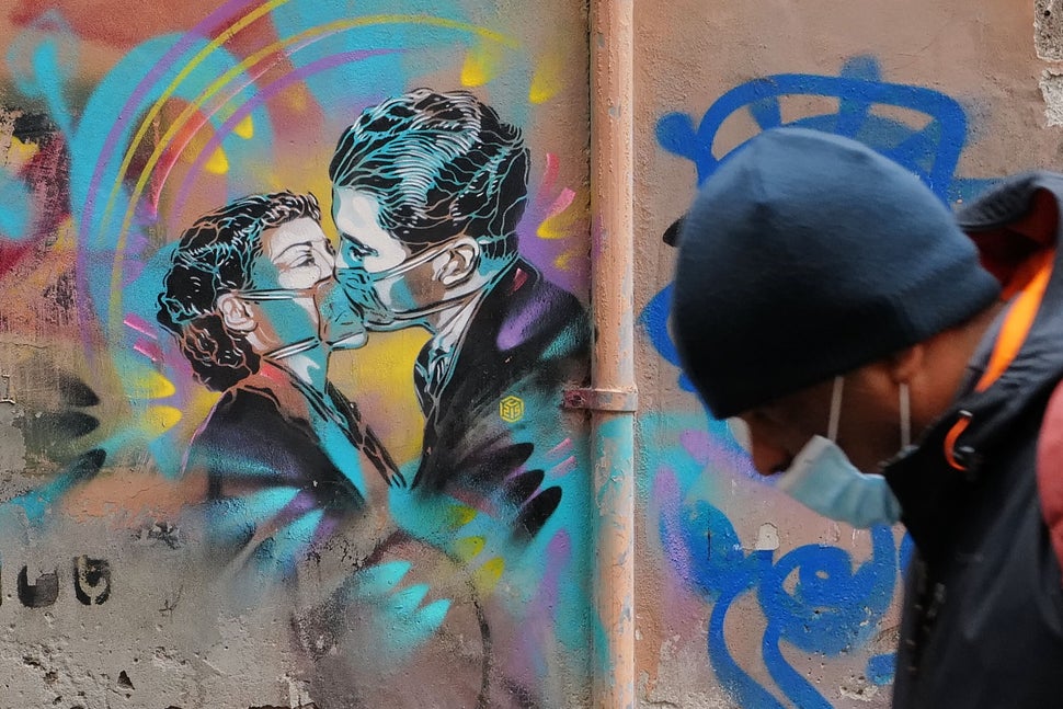 A pedestrian wearing a protective face mask walks past graffiti depicting a couple kissing wearing protective masks, in centr