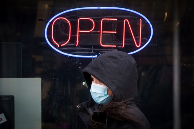 A person wears a mask to protect them from the COVID-19 virus while walking past an open sign in Kingston,...