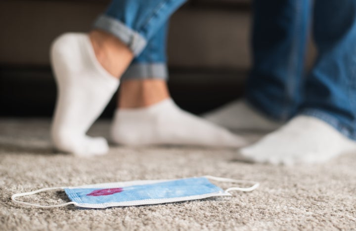 Protective face mask with kiss mark on the floor, loving couple feet on background. Saint valentine's day 2021