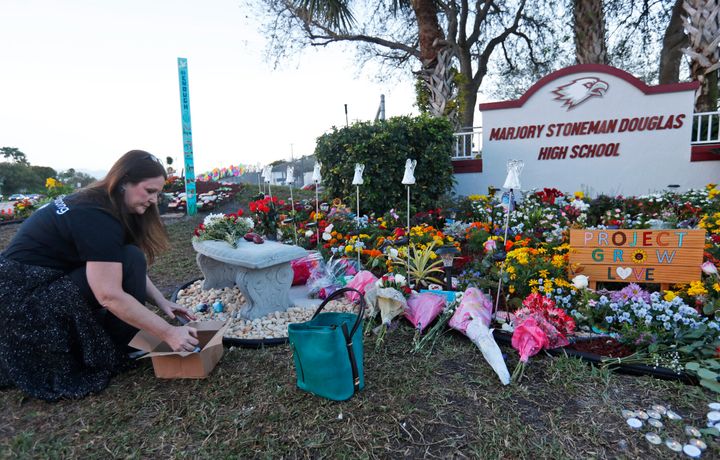 Suzanne Devine Clark, an art teacher at Deerfield Beach Elementary School, places painted stones at a memorial outside Marjory Stoneman Douglas High School during the first anniversary of the school shooting in 2019.