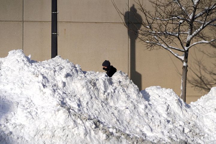 A man walks past mounds of plowed snow from nine consecutive days of measurable and fresh fallen snow Tuesday, Feb. 16, 2021, in Chicago. (AP Photo/Charles Rex Arbogast)