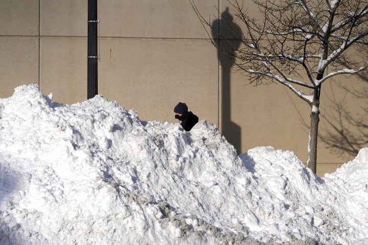 A man walks past mounds of plowed snow from nine consecutive days of measurable and fresh fallen snow Tuesday, Feb. 16, 2021,