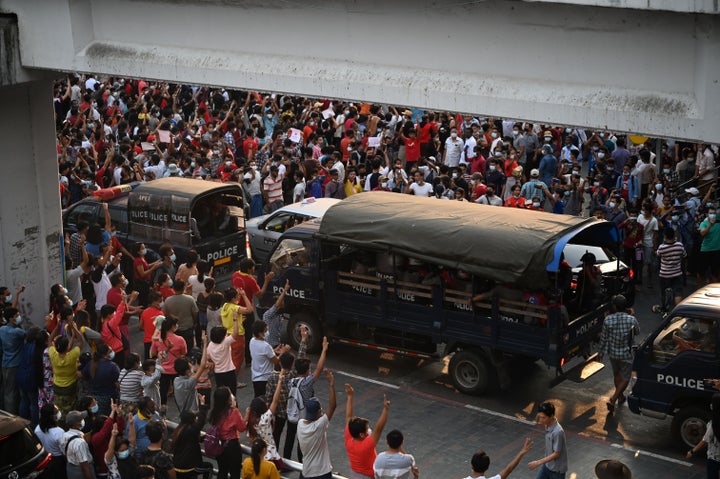 Protesters hold up the three finger salute towards trucks carrying police making their way through a demonstration against the military coup in Yangon on February 6, 2021.