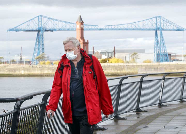 A man wearing a face mask walks by the Tees Transporter Bridge in Middlesbrough last October. 