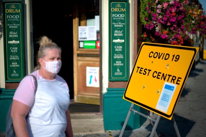 Pedestrians wearing a facemask walking past a sign for a Covid-19 test centre in Leyton, east London