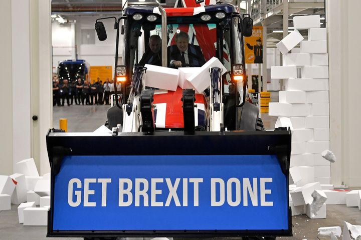Boris Johnson drives a Union flag-themed JCB, with the words "Get Brexit Done" inside the digger bucket, through a fake wall emblazoned with the word "GRIDLOCK".