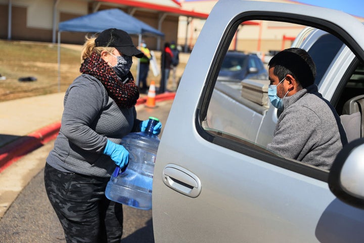 KYLE, TEXAS - FEBRUARY 20: Erin Purdy gives Domingo Ibarra a water jug at a drive through water distribution center setup at 