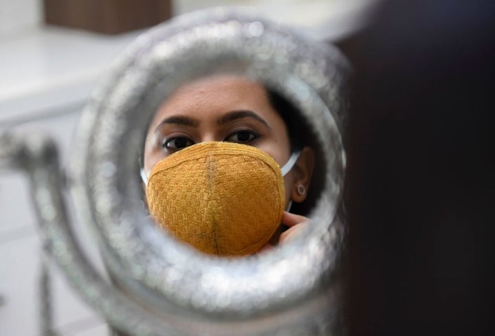 Una mujer se mira al espejo mientras se ajusta su mascarilla