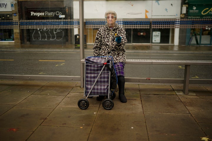 A woman wears a face shield as she sits at a bus stop in Sheffield last October