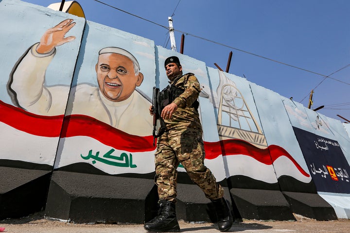 A member of the Iraqi forces walks past a mural depicting Pope Francis waving next to an Iraqi national flag drawn on a blast wall outside the Syriac Catholic Church of Our Lady of Deliverance in the Karrada district of Iraq's capital Baghdad on March 1, 2021 amidst preparations ahead of the pontiff's visit. 