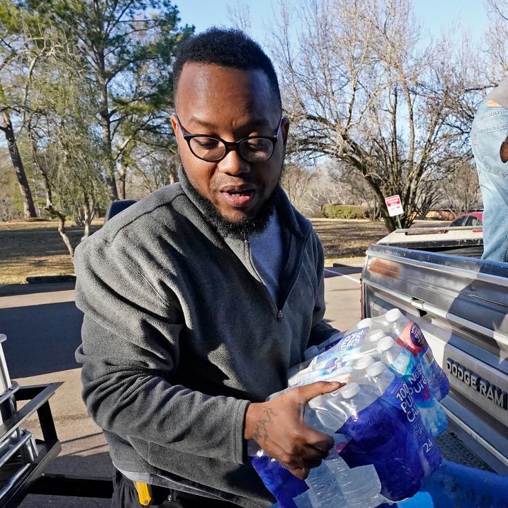 Lamar Jackson, left, stacks bottled water brought by Mac Epps of Mississippi Move at a senior residence in Jackson, Mississippi, on Feb. 22, 2021. Rising temperatures have melted the snow and ice in Mississippi, but tens of thousands of people still had little or no water service.