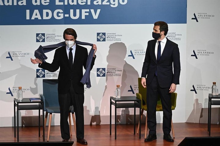 El expresidente del Gobierno, José María Aznar, se quita la bufanda bajo la atenta mirada del presidente del PP, Pablo Casado.