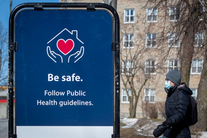 A person wears a mask to protect them from the COVID-19 virus, as they walk by a poster to follow public health guidelines, in Kingston, Ont. on Tuesday.
