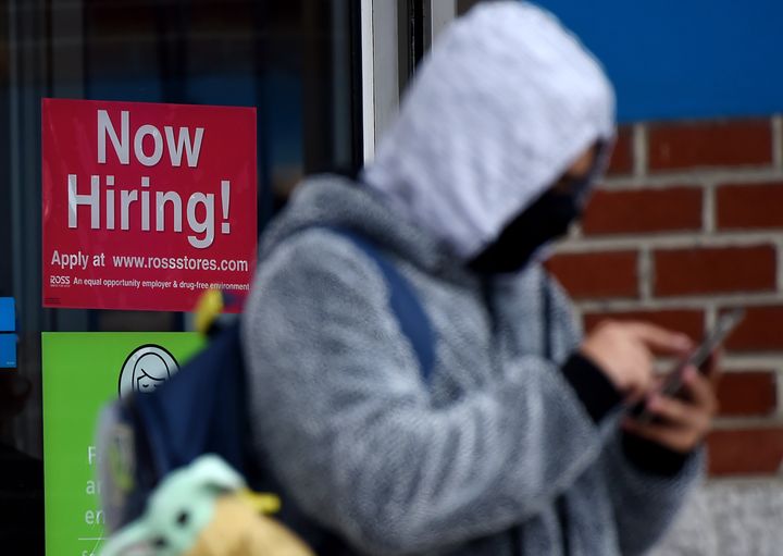 A man wearing a face mask stands next to a "Now Hiring " sign in front of a store in Arlington, Virginia, on Dec. 18.