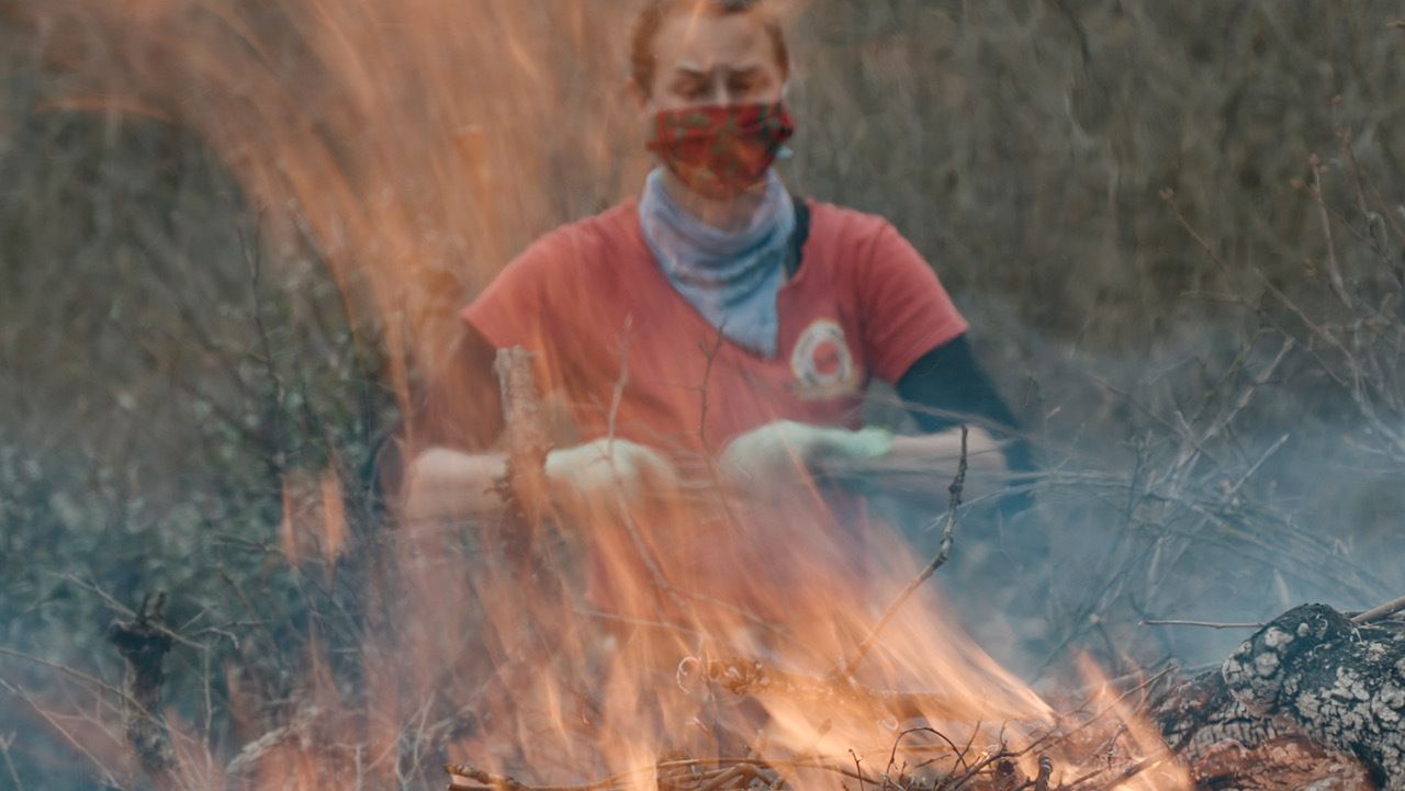 Stephanie Beard, the communication specialist for the conservation nonprofit Pepperwood, throws more dried brush on a flaming burn pile.