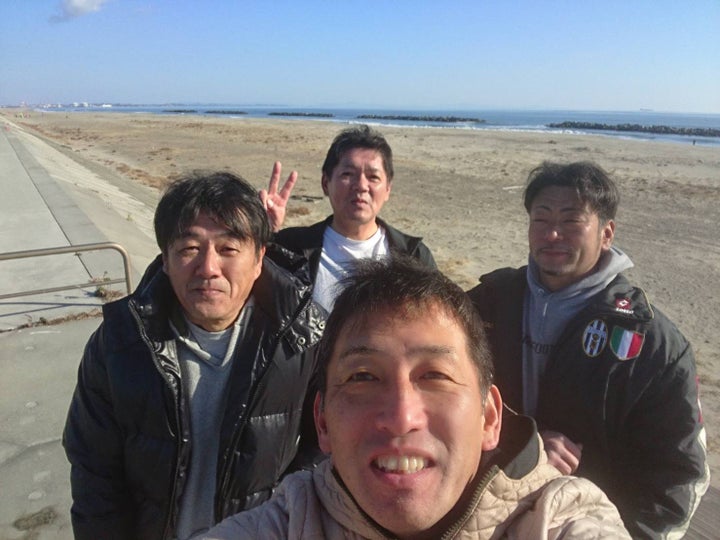 サーフィンを楽しんだ後に荒浜の海岸で仲間と写真に収まる前之濱さん（中央手前）と末永さん（中央後方）＝2019年12月、前之濱さん提供