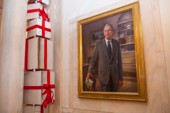 In the Cross Hall of the White House, holiday decorations feature stacked columns of shiny presents next to the official port