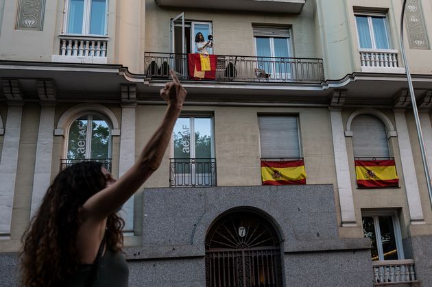 Una mujer protesta con una cacerola desde su balcón contra las restricciones, mientras otra le hace una...