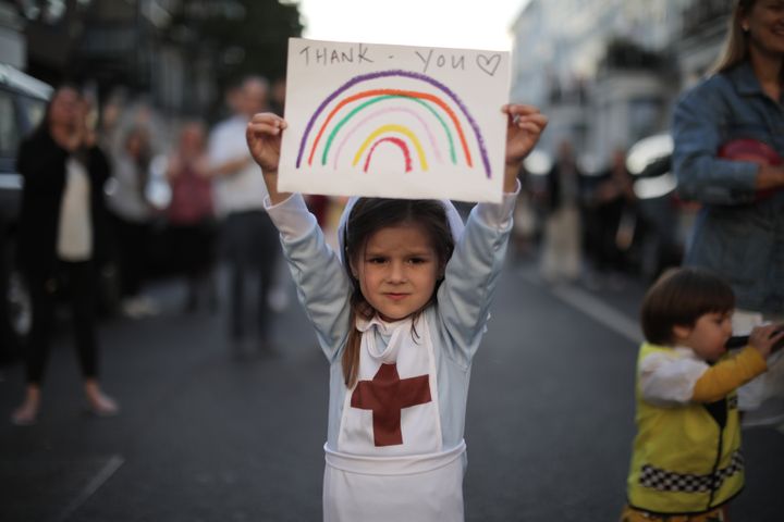Maria Sole, 4, dressed in a small nurses outfit holds up a rainbow drawing with the words 'Thank You'