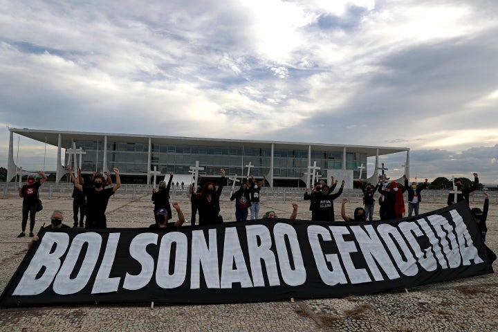 Demonstrators hold crosses to represent people who have died of COVID-19 behind the Portuguese phrase "Bolsonaro genocide" as