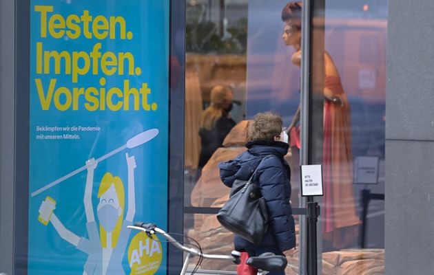 Une femme avec un masque passe devant des boutiques à Berlin, le 29 mars 2021. Sur le panneau à côté figure le slogan; 