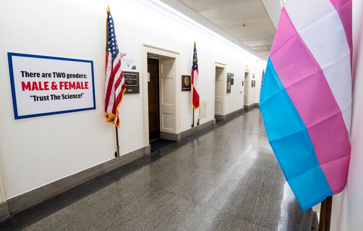 The transgender pride flag hangs across the hall from a transphobic sign outside the office of Rep. Marjorie Taylor Greene (R