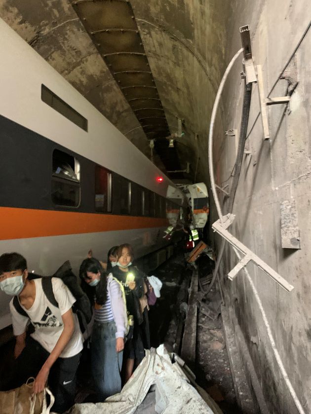 People walk next to a train which derailed in a tunnel north of Hualien