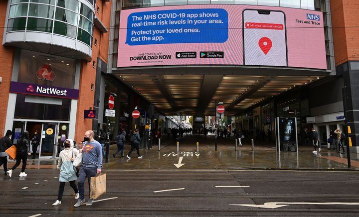 Shoppers pass beneath an electronic sign promoting the NHS Covi-19 app, outside the Arndale Centre in Manchester.