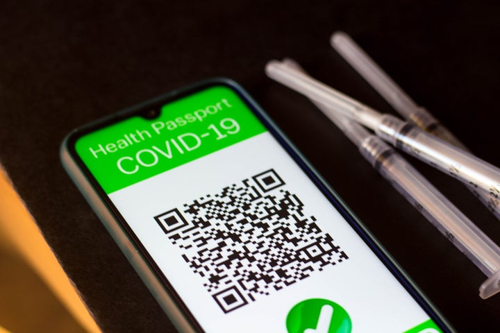 In this photo illustration a symbolic Covid-19 health passport seen on a smartphone screen next to the medical syringes