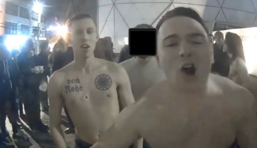 McCaffrey, shirtless, yells into a camera at an art exhibit at the Museum of the Moving Image in Queens, New York, in February 2017. Next to him is a man with a chest tattoo of a sonnenrad.